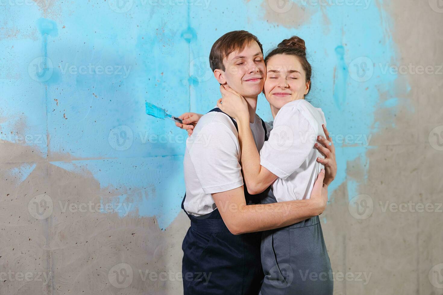 House decoration DIY renovation concept. Happy couple during repair in empty room of new home painting wall together. Husband and wife hugging in new house. Happy family doing home renovation. photo