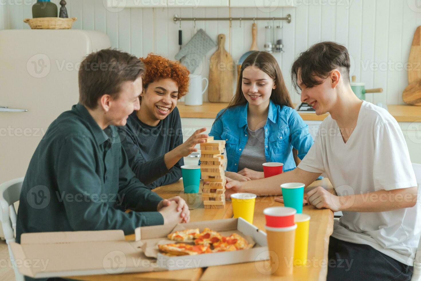 Home party. Friends spending time together playing in board game crash wooden tower at home. Happy diverse group having fun together indoor. Mixed race young buddies best friends enjoying weekend. photo