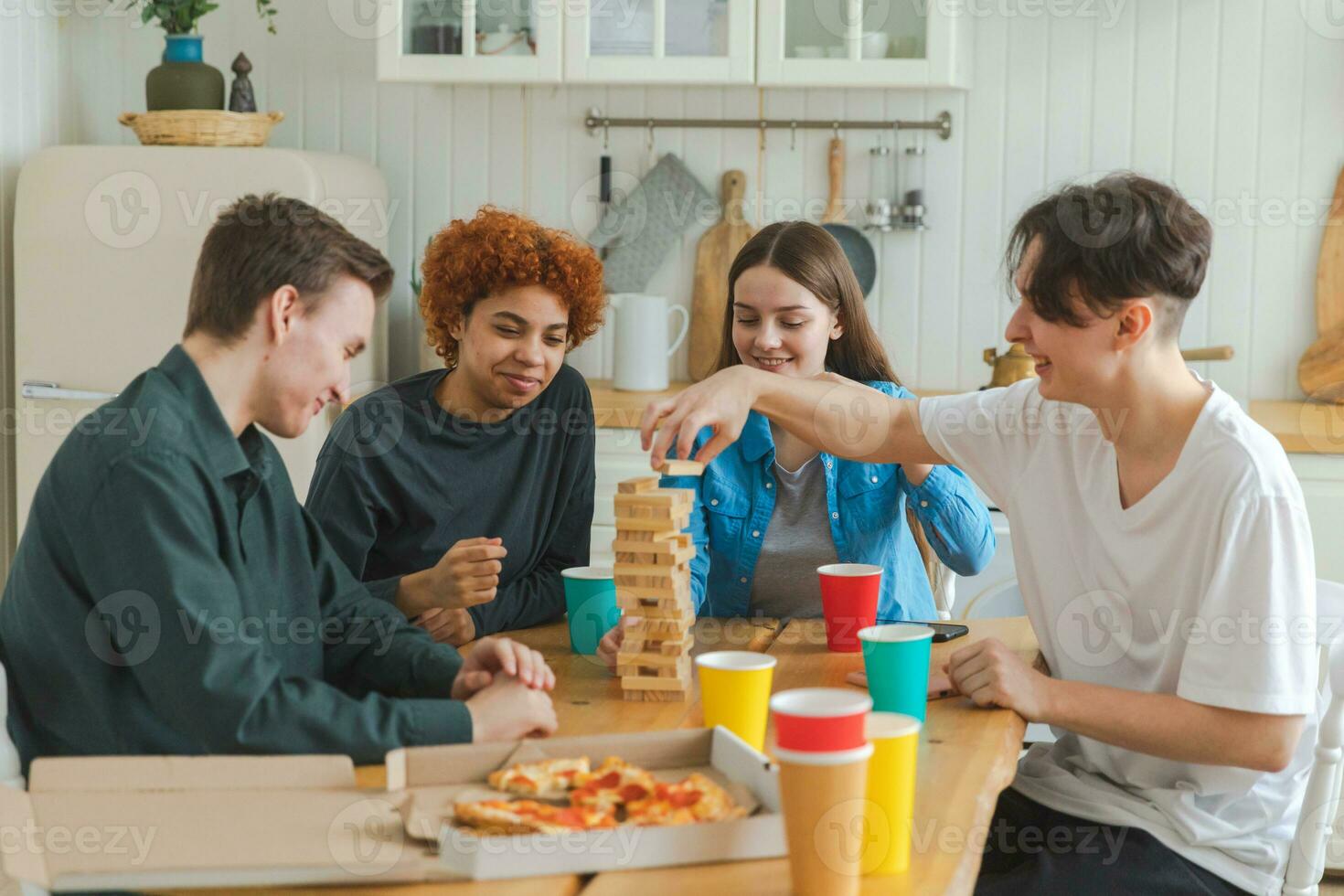 Home party. Friends spending time together playing in board game crash wooden tower at home. Happy diverse group having fun together indoor. Mixed race young buddies best friends enjoying weekend. photo