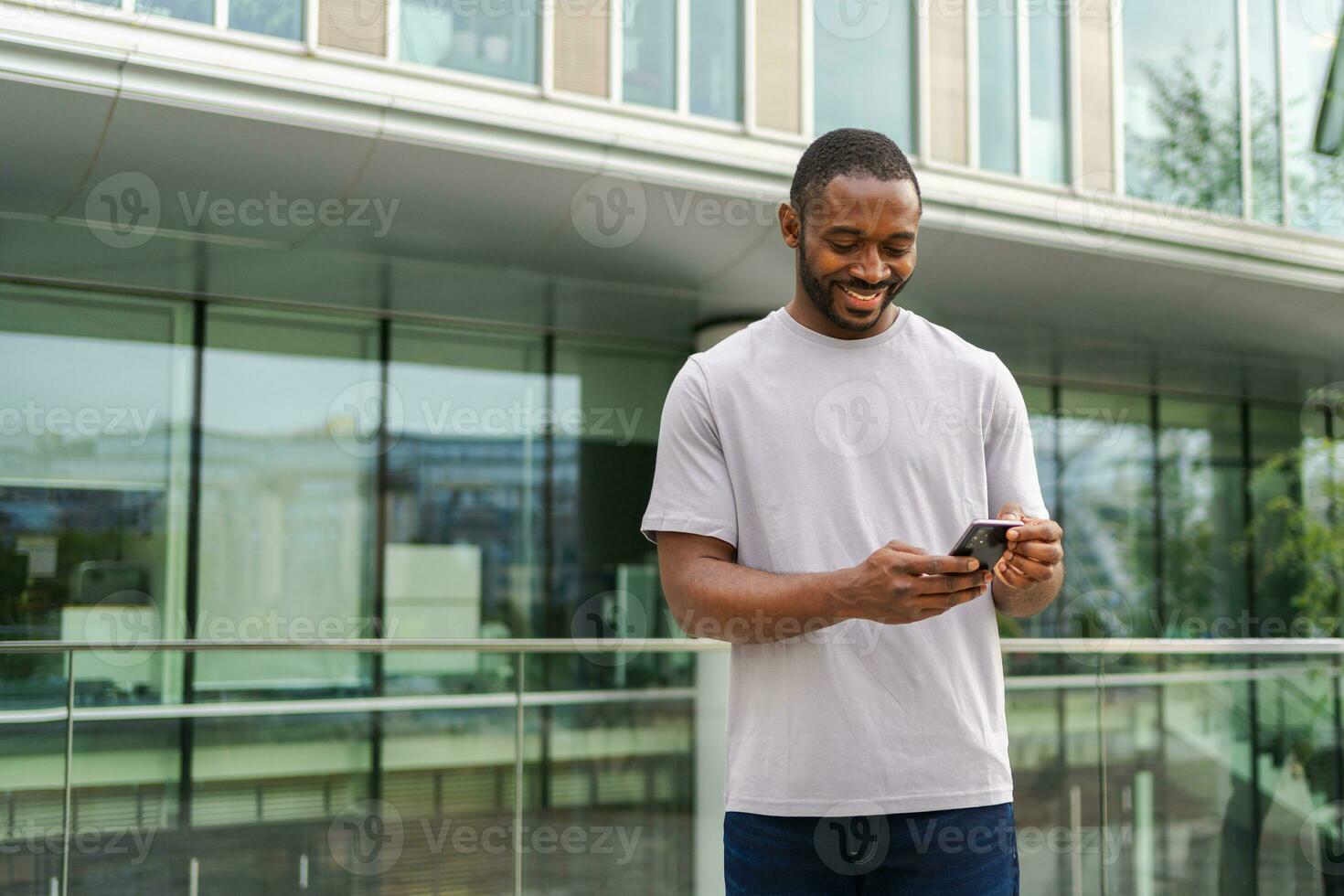 African american man holding smartphone touch screen typing scroll page on urban street in city. Guy with cell phone surfing internet using social media apps shopping online. Cellphone addiction. photo