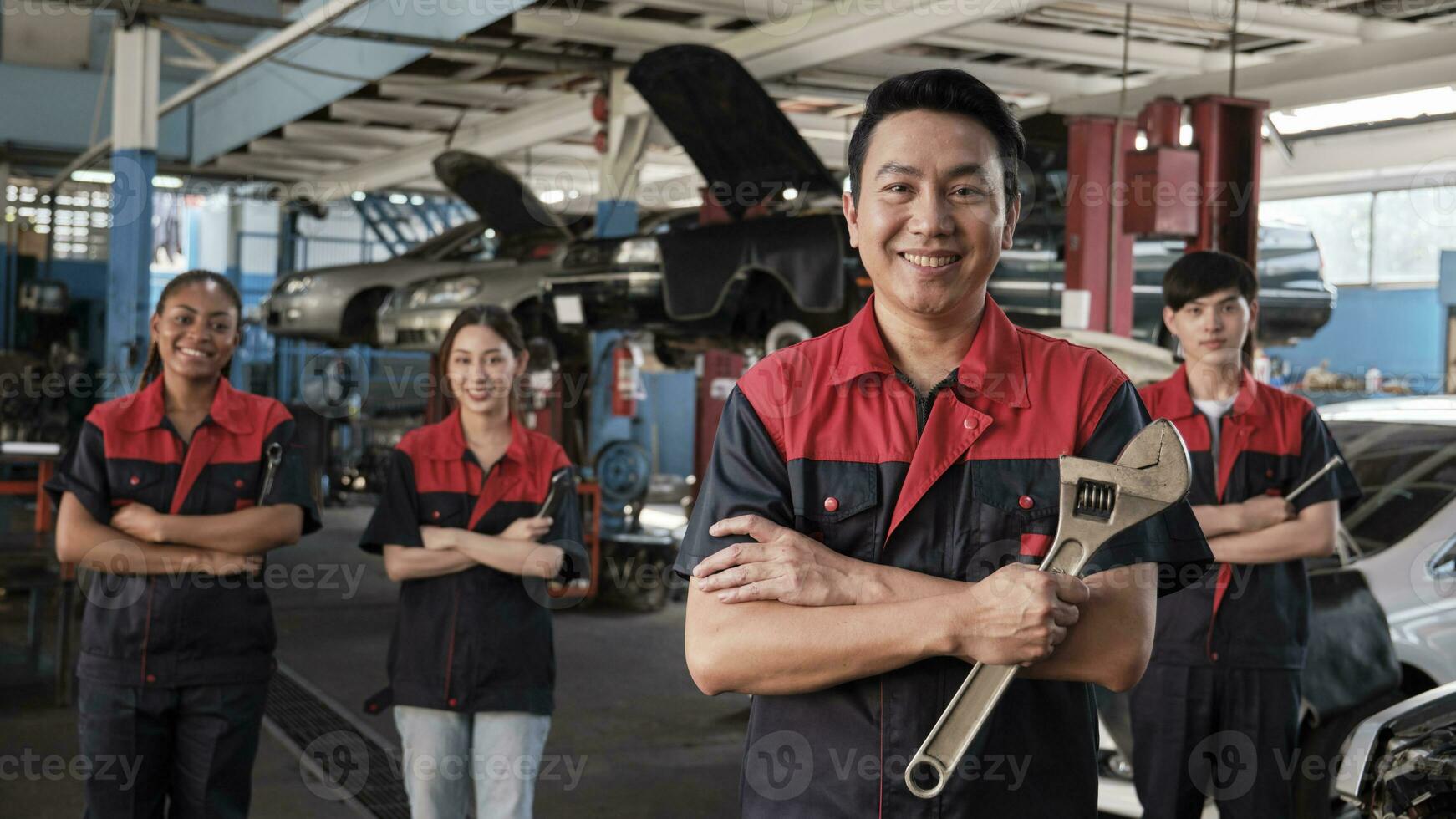Portrait of professional workers team, male Asian supervisor arms crossed with fixing tools in front of mechanic colleagues, guarantee car repair jobs success with cheerful smiles at service garage. photo