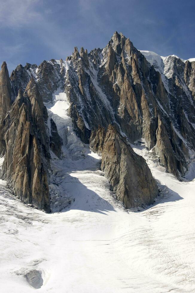 dos personas son excursionismo arriba un montaña con nieve cubierto montañas foto