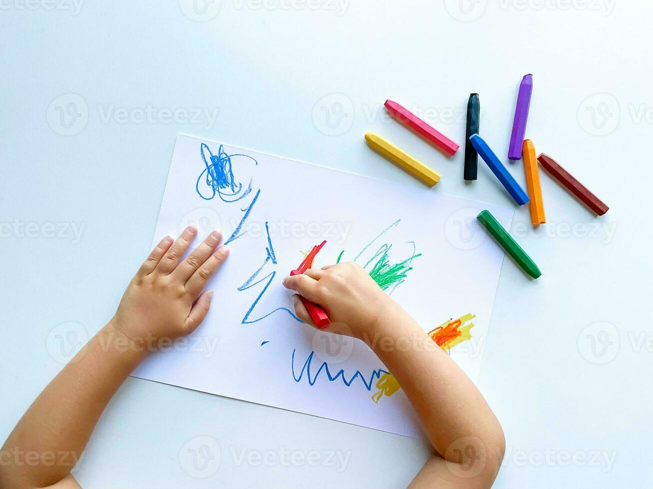 small child draws with pastel crayons on white table. photo