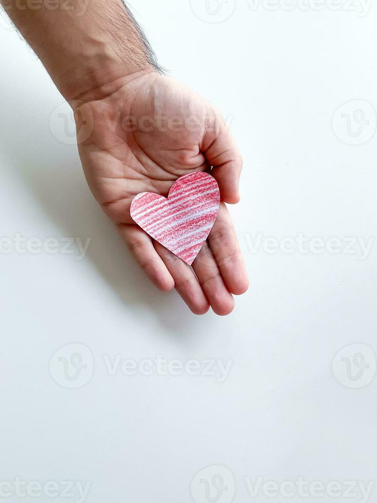 A mans hand holds a red paper heart on a white background. Empty space for an inscription. The concept of manifestation of love. photo