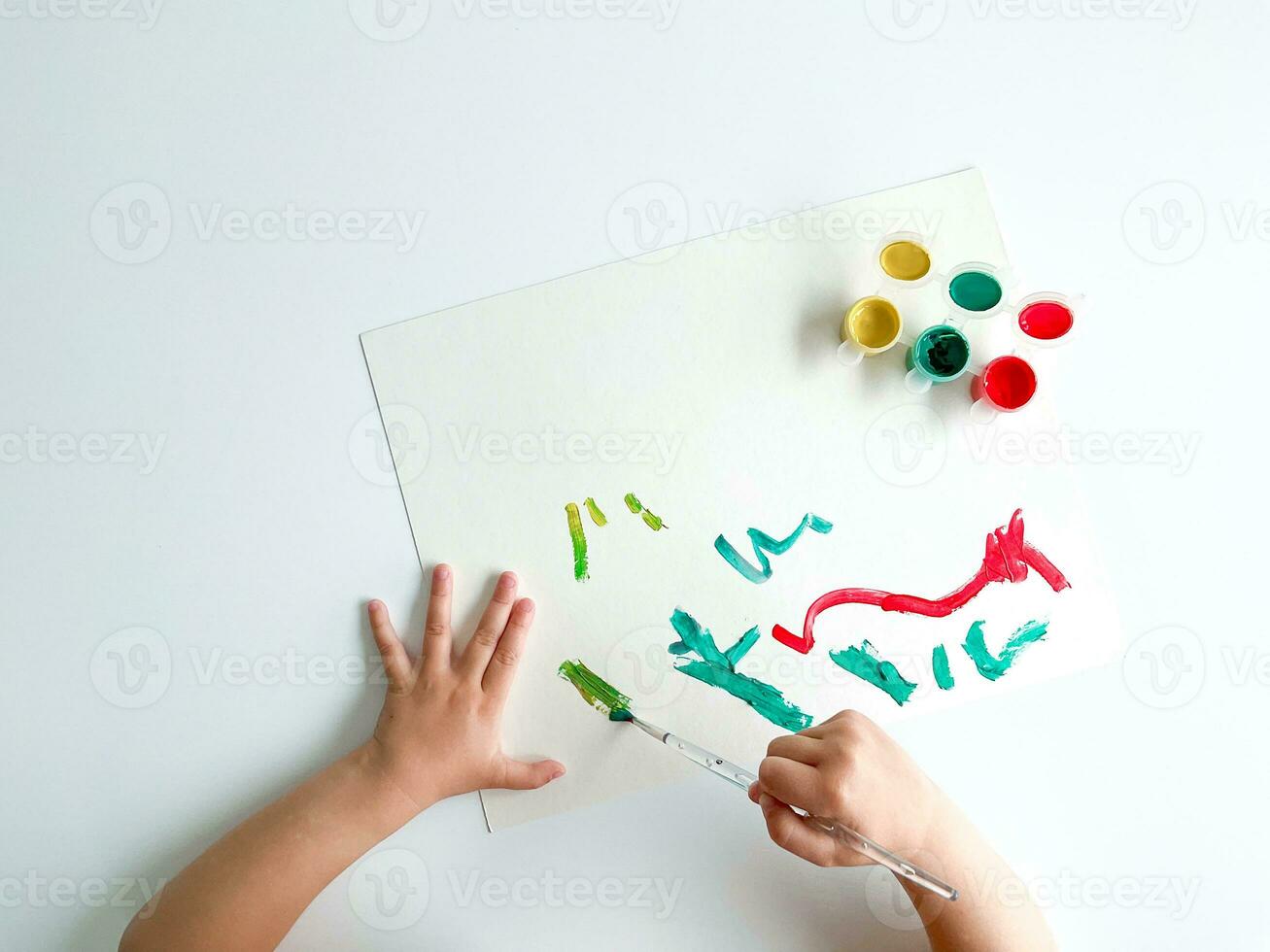 pequeño niño sorteos con pinturas y cepillo en blanco mesa. foto