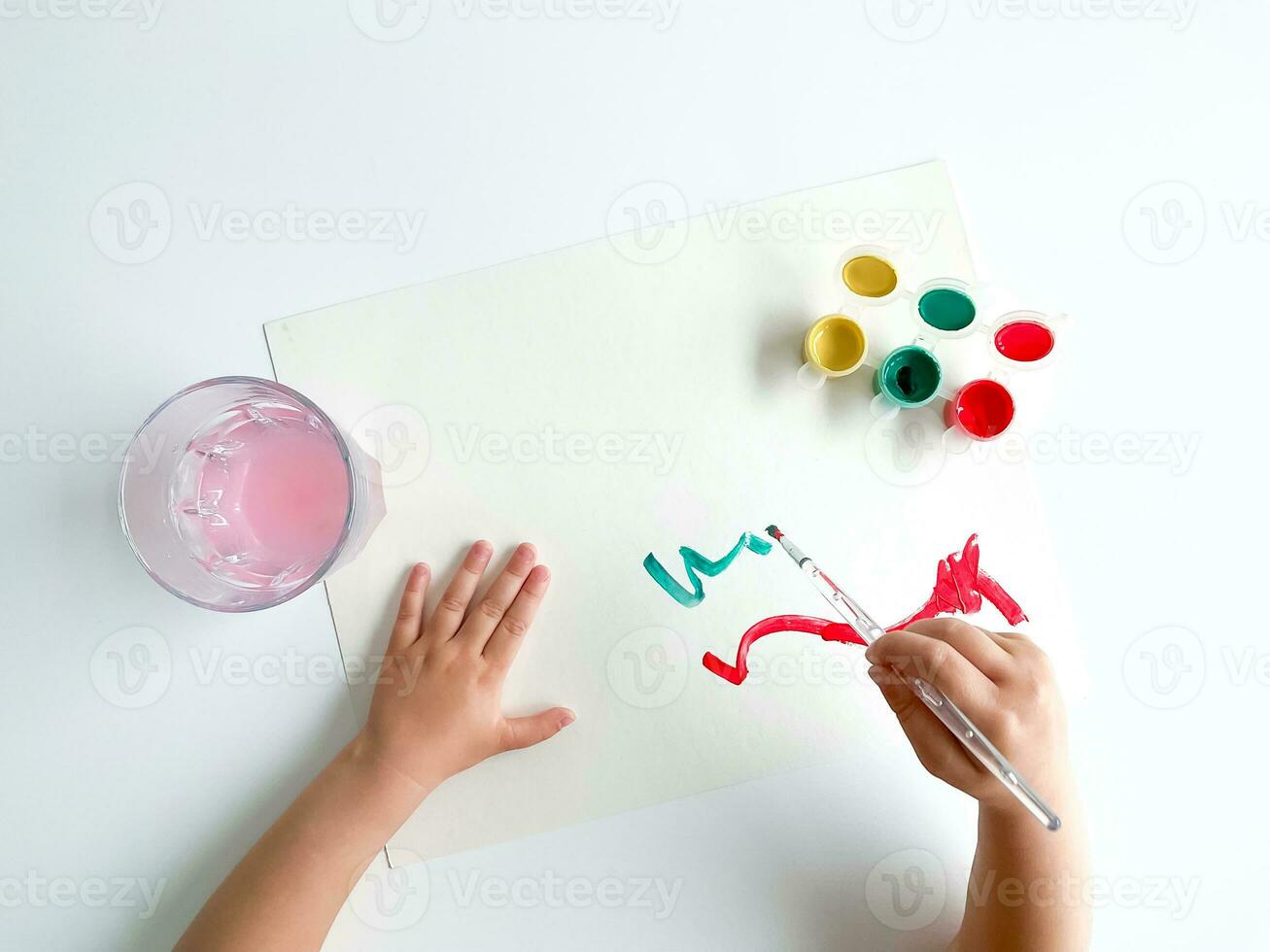 small child draws with paints and brush on white table. photo