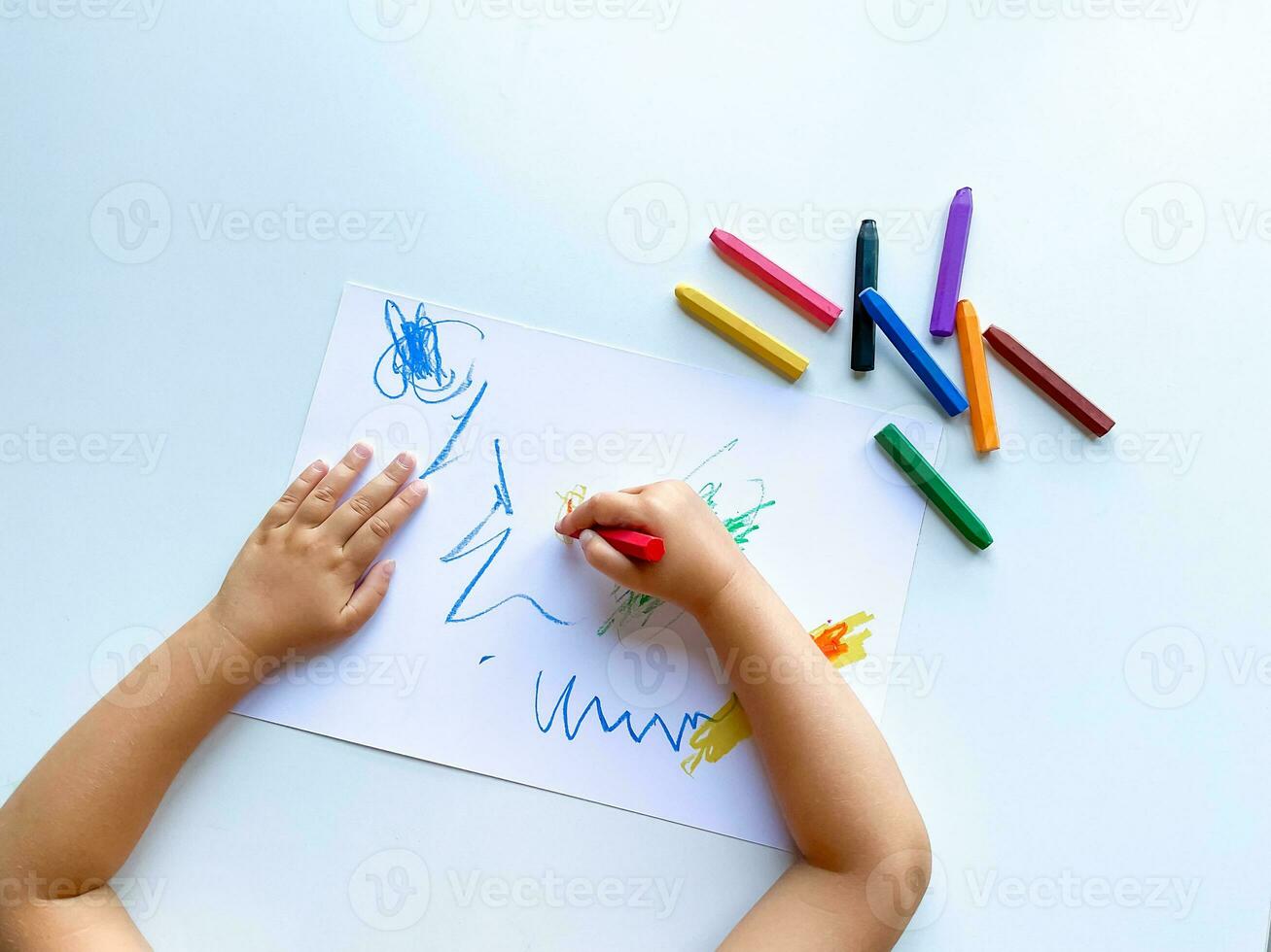 small child draws with pastel crayons on white table. photo