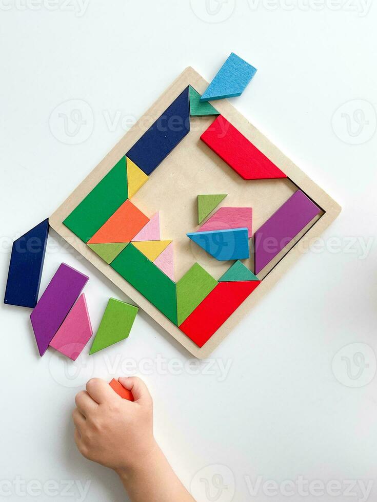 childs hand collects multicolored wooden mosaic on white background. photo