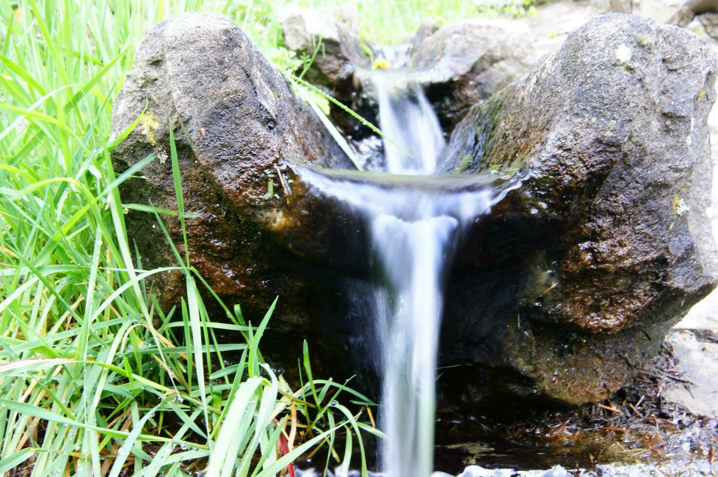 a small waterfall flowing out of a rock photo