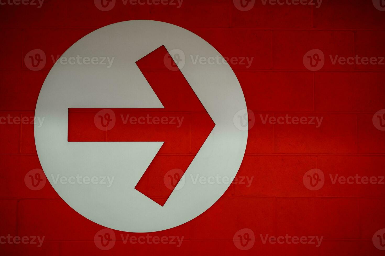 Arrow sign in white circle on red brick wall background, Directional Arrow  pointing to right side photo