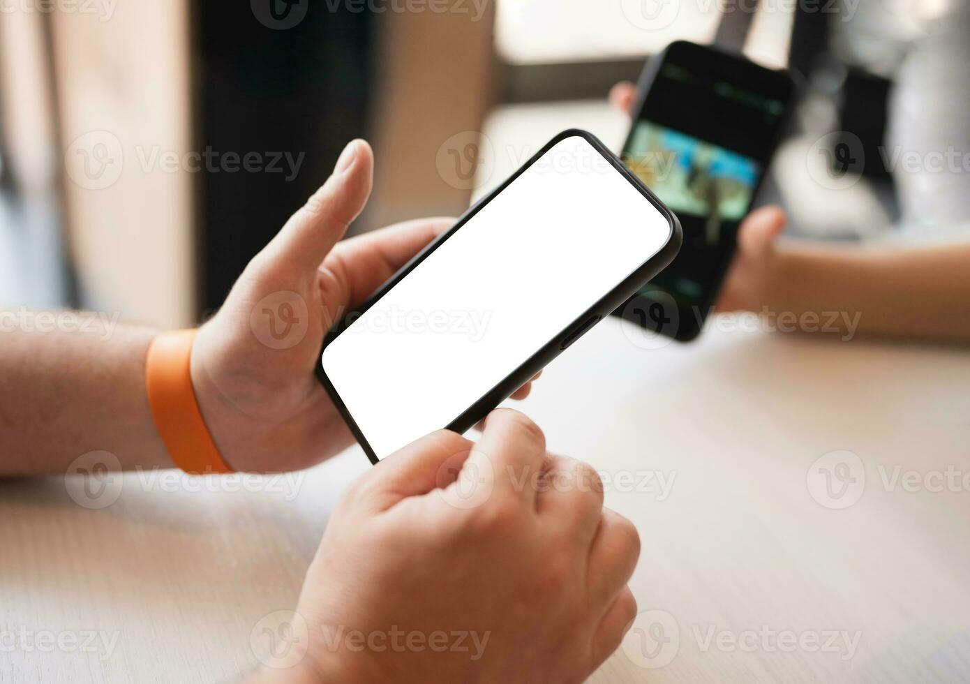 Cropped shot view of man hands holding Smart phone with blank copy space screen for your text message or information content with blurry kid hand showing mobile phone behind photo