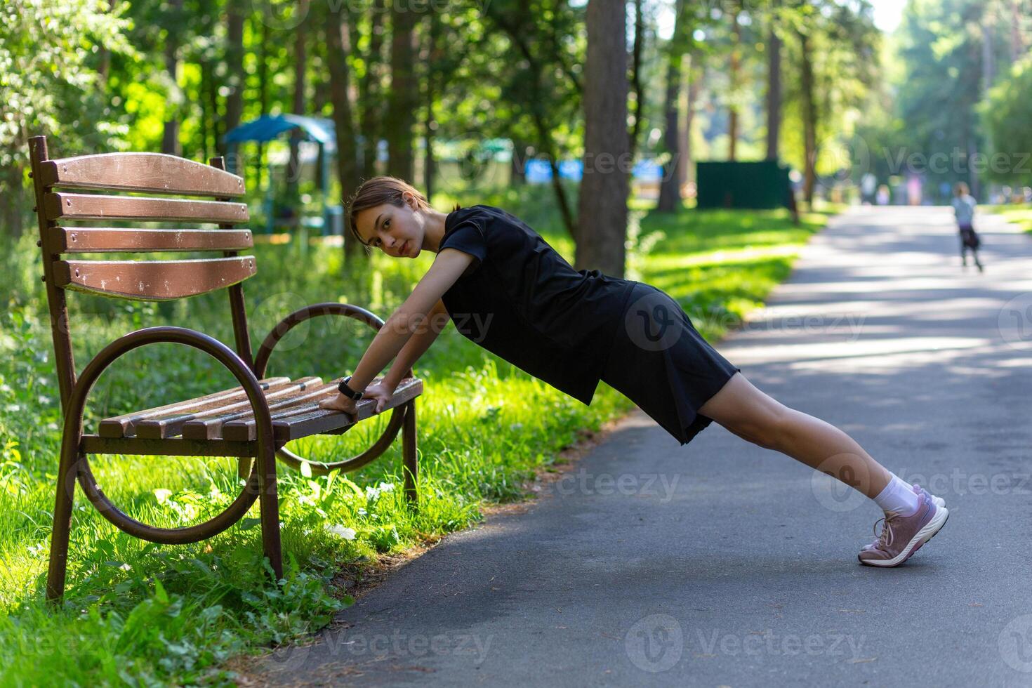 hermosa joven deportivo mujer en negro camiseta, negro pantalones cortos y rosado entrenadores calentamiento arriba hacer ejercicio triceps y cofre foto