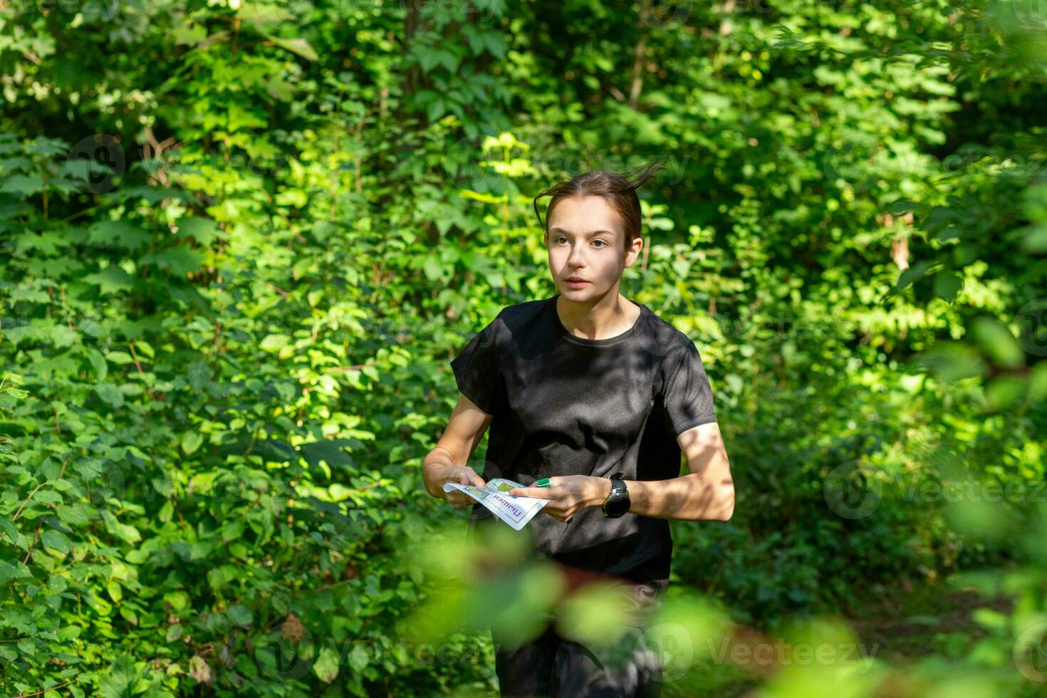 Young girl in forest reading map and searching for a control point. Sports orienteering competition. photo