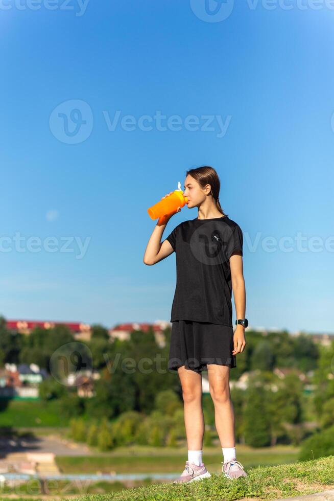 Fit tennage girl runner outdoors holding water bottle. photo