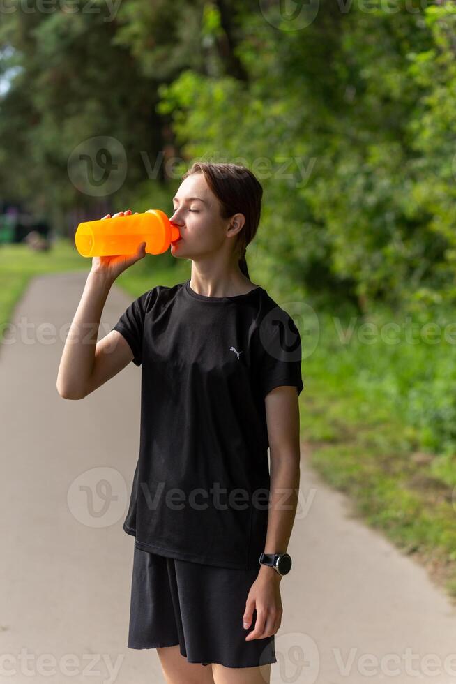 Fit tennage girl runner outdoors holding water bottle. photo