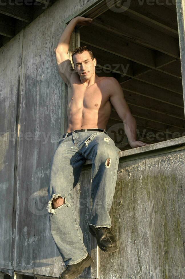 A hot male strips off his shirt to pose in a barn window showing off his muscular body. photo