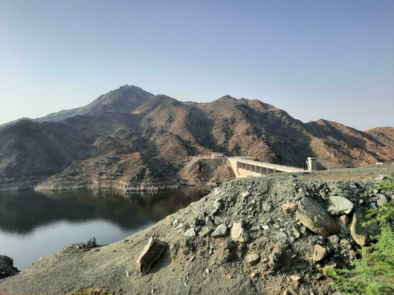 A beautiful daytime view of  Wadi Qanuna Dam in Al Bahah, Saudi Arabia. The water of the dam and the surrounding hills are presenting a beautiful scene in the sunlight. photo