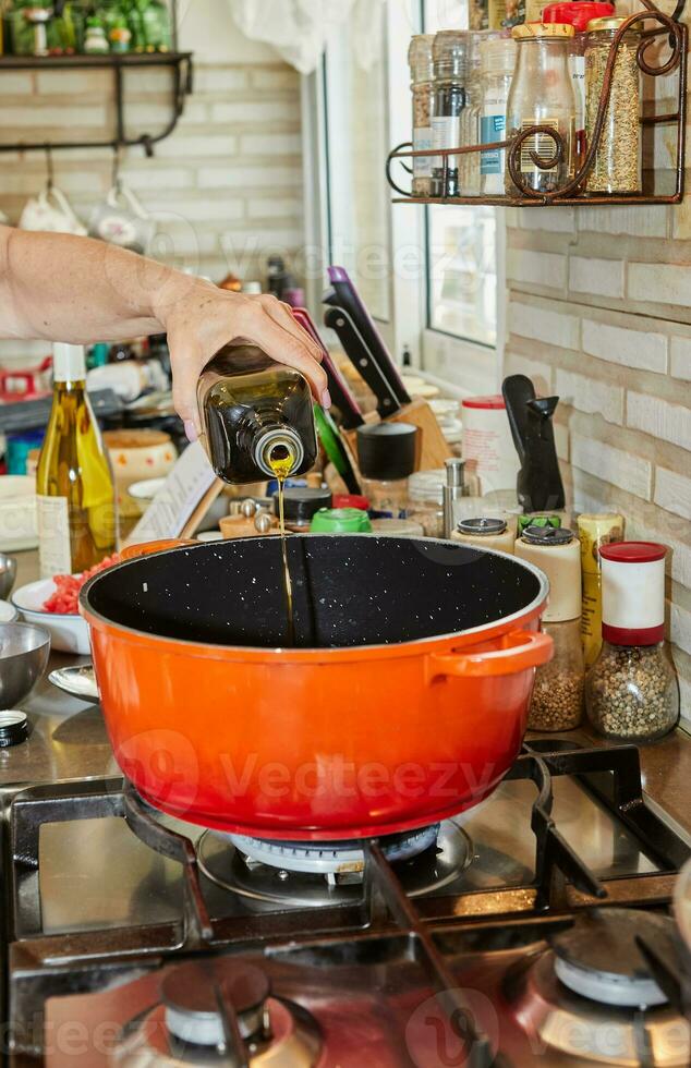 Chef pouring olive oil into pan on gas stove photo