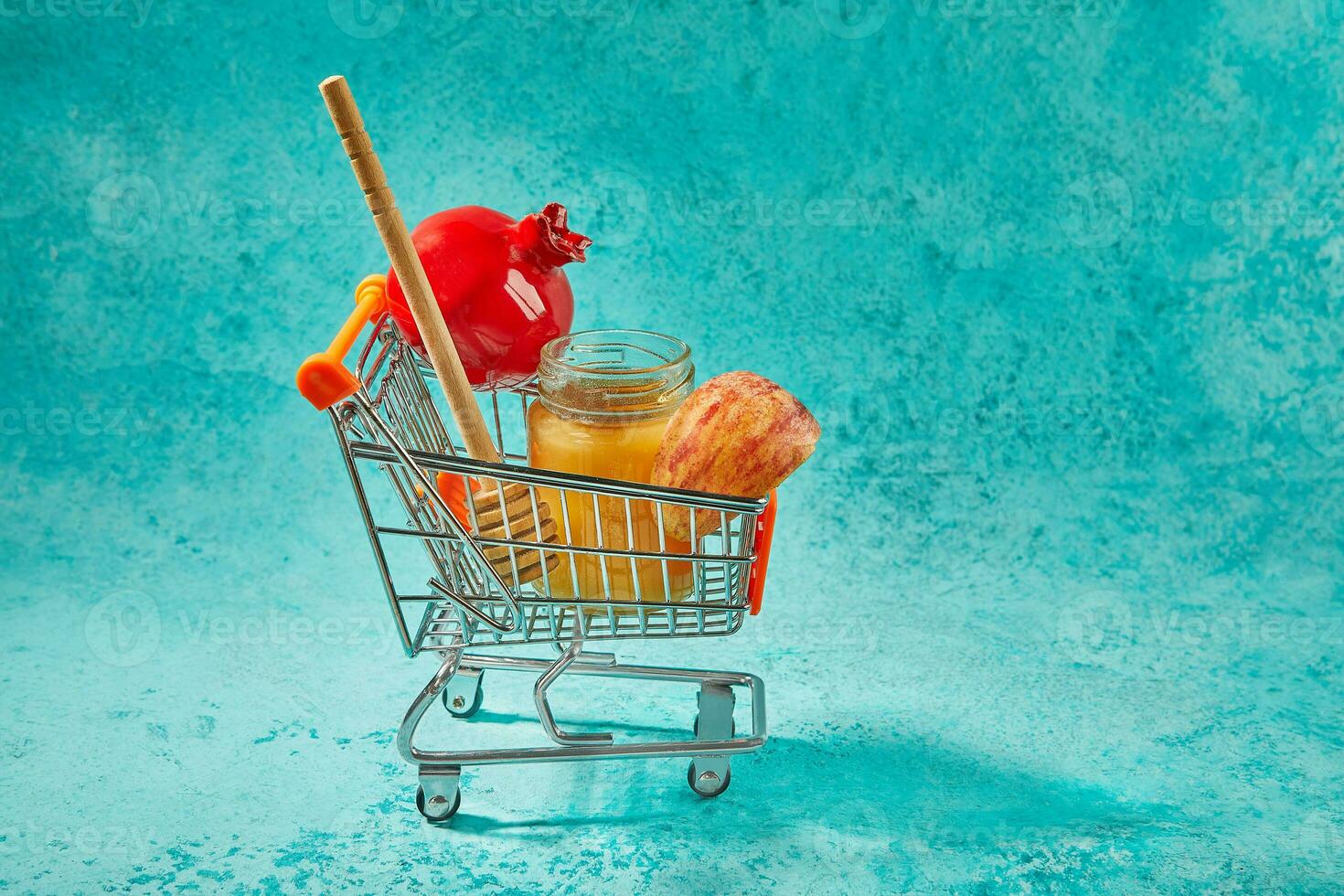 Rosh hashanah - jewish new year holiday concept. Bowl in the shape of an apple with honey, apples, pomegranates, shofar on blue background in a cart photo