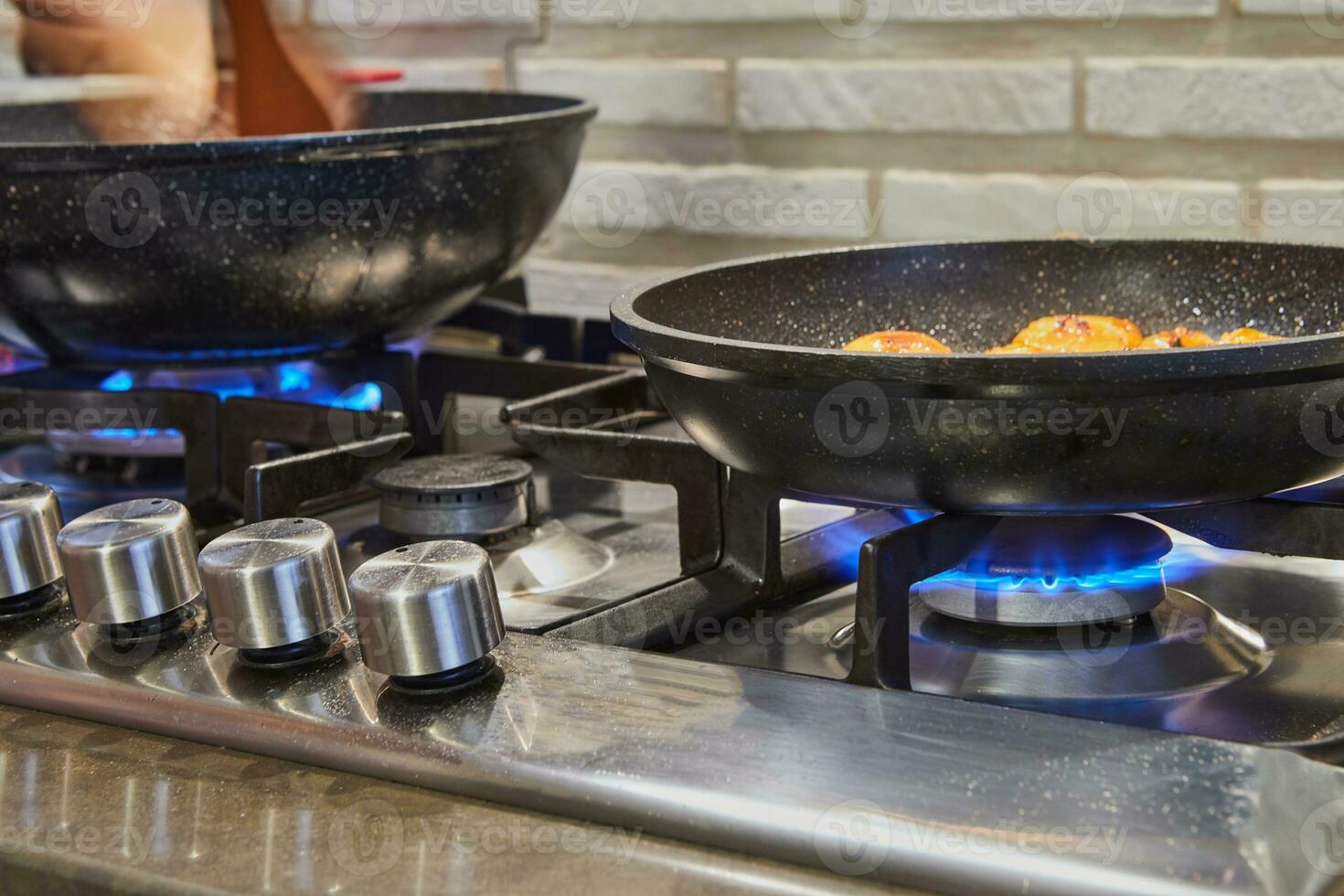 Frying pans on burner fire on gas stove with dish being prepared photo