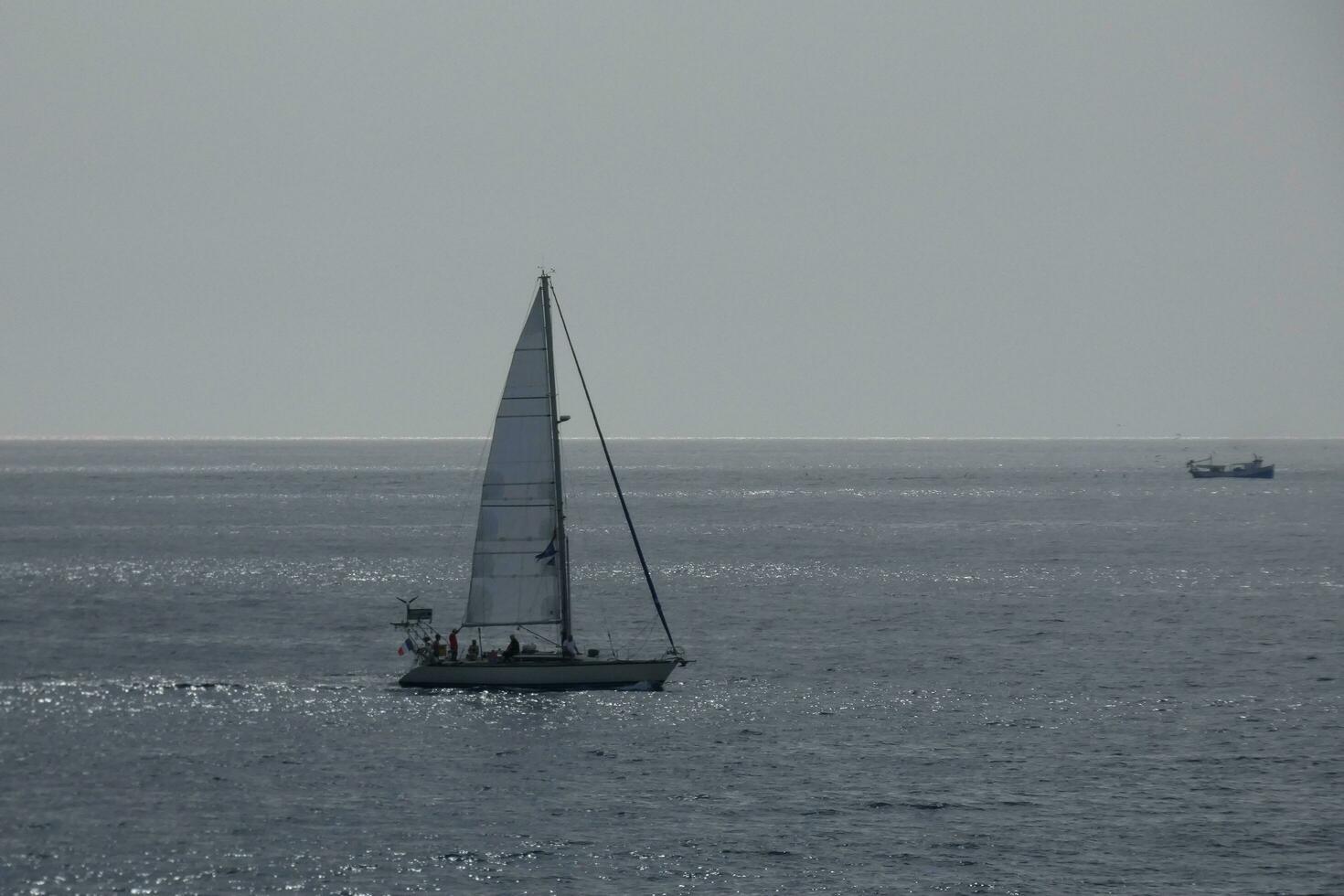 Sailboat with sail unfurled, sailing on the calm sea at sunset. photo