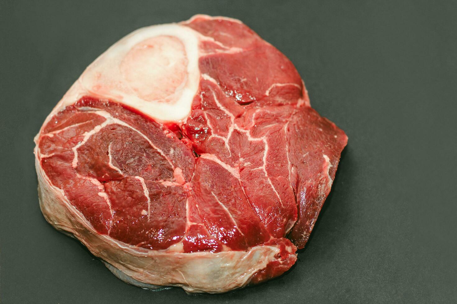 Fresh piece of meat large beef steak on the bone ossobuco with a sprig of rosemary on a black background photo