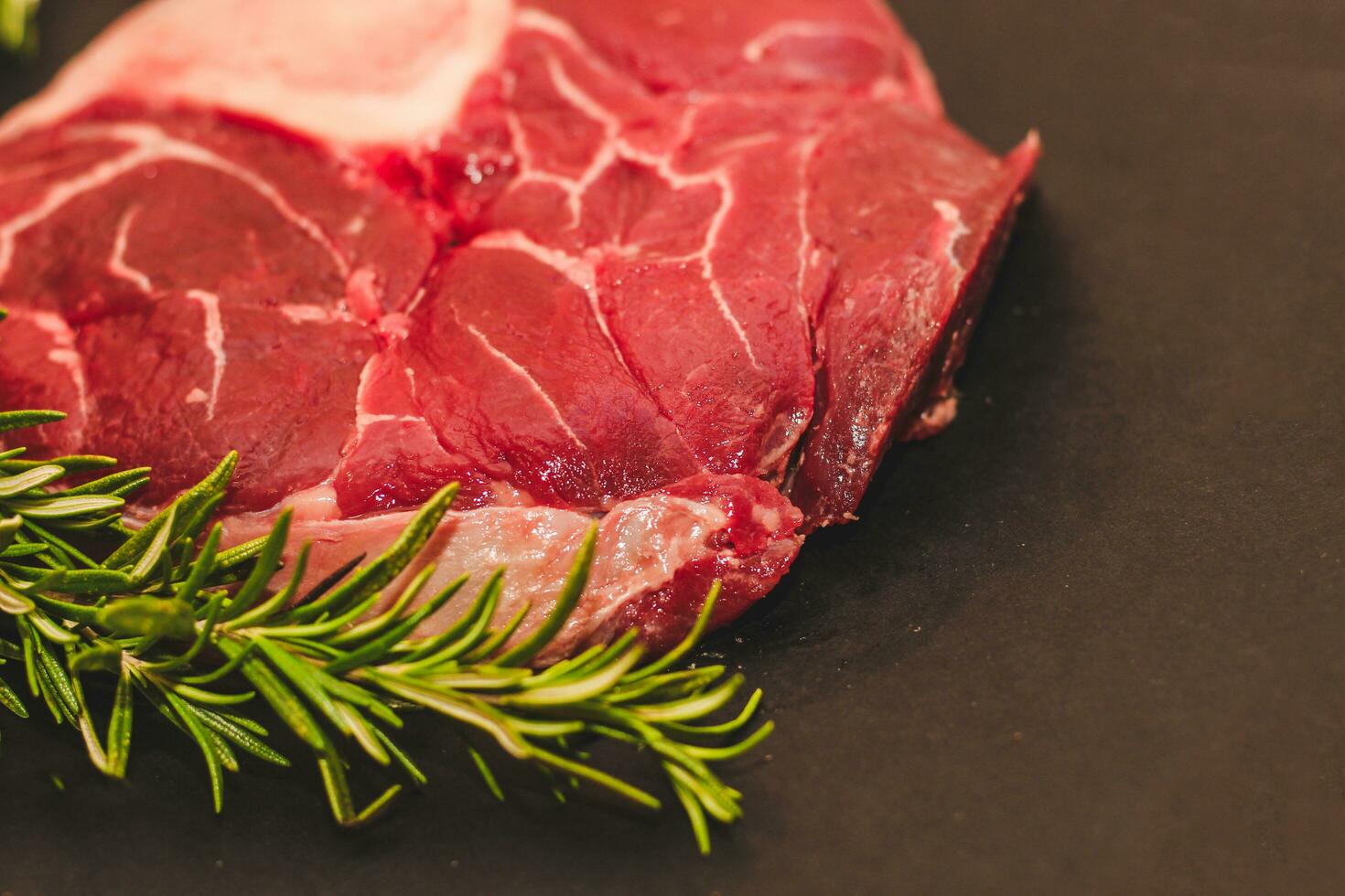 Fresh piece of meat large beef steak on the bone ossobuco with a sprig of rosemary on a black background photo