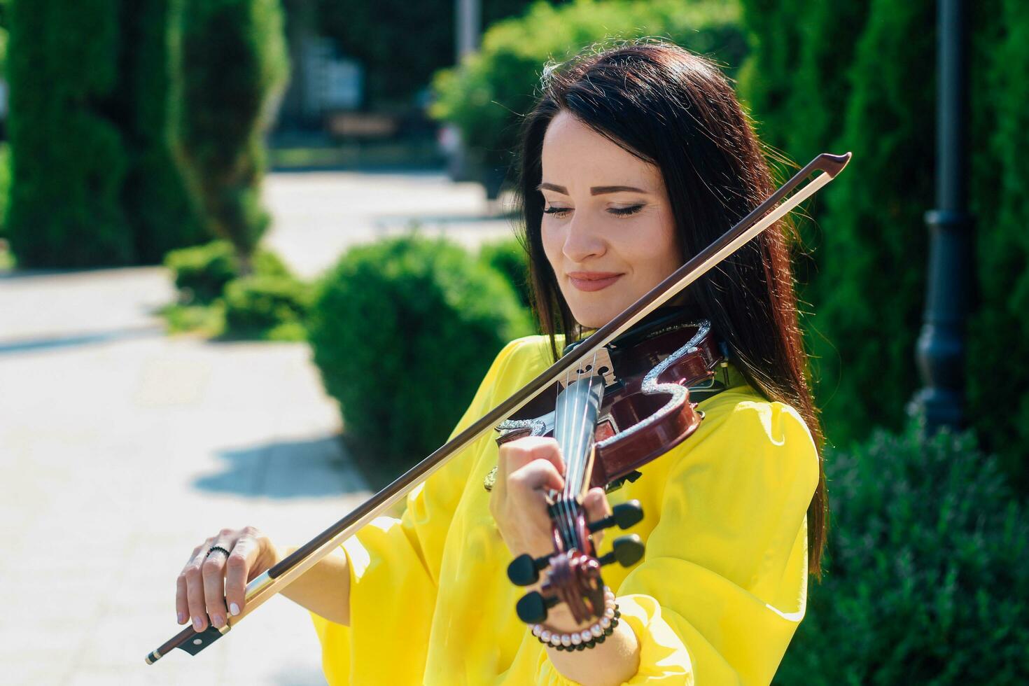 Woman artist with dark hair in a dress plays a wooden concert electric violin photo