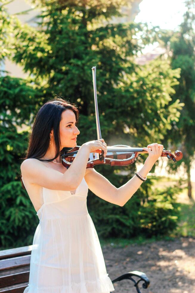 Woman artist with dark hair in a dress plays a wooden concert electric violin photo