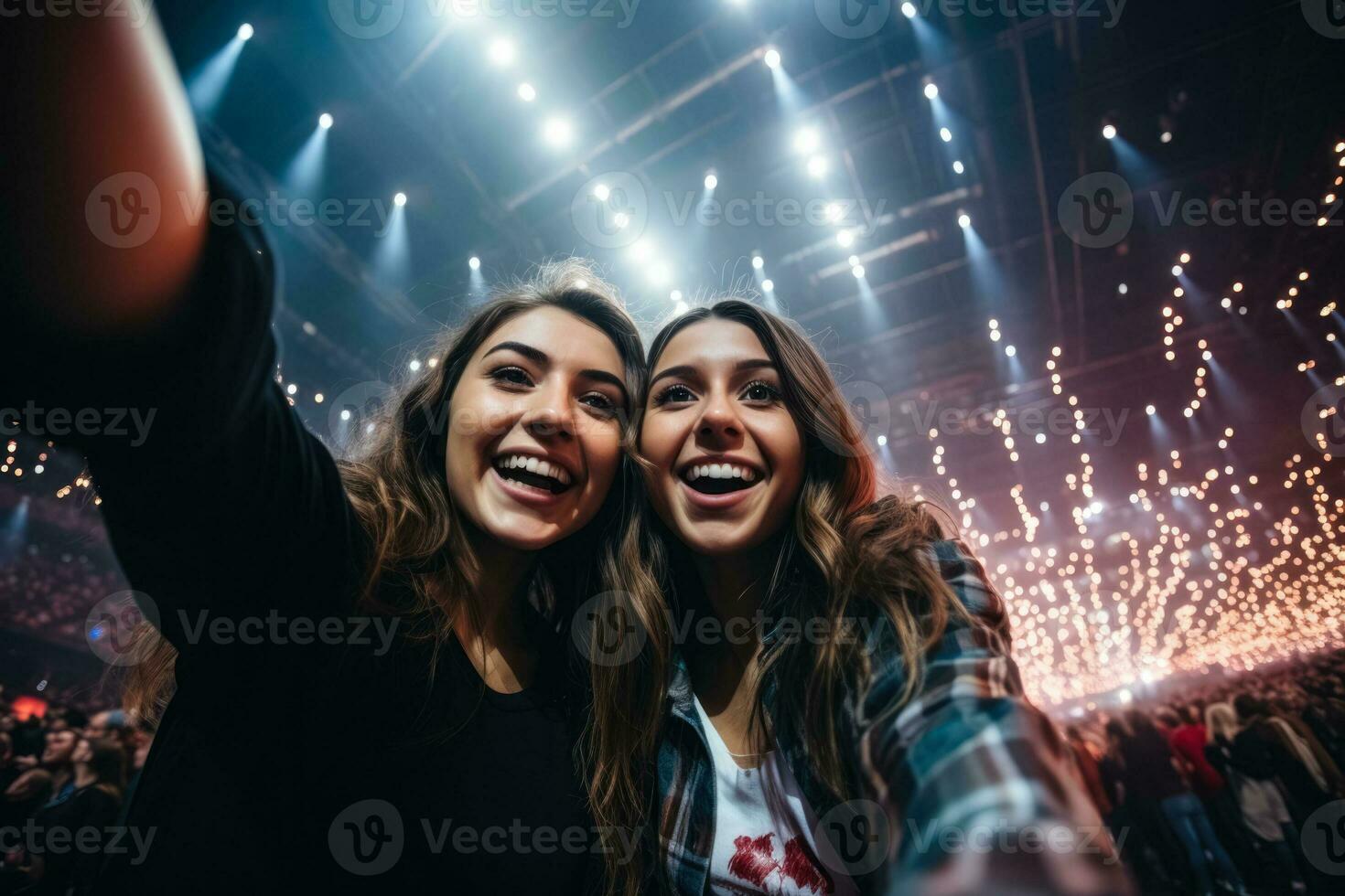 Two young women at concert capturing selfie in massive indoor arena photo
