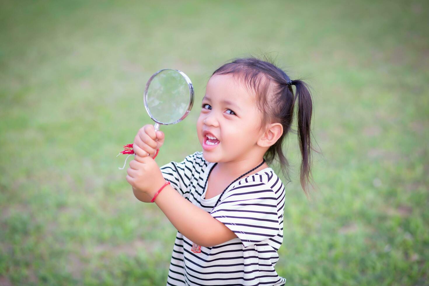 Asian little girl is using magnifying glass to play in the park.SSTKHome photo
