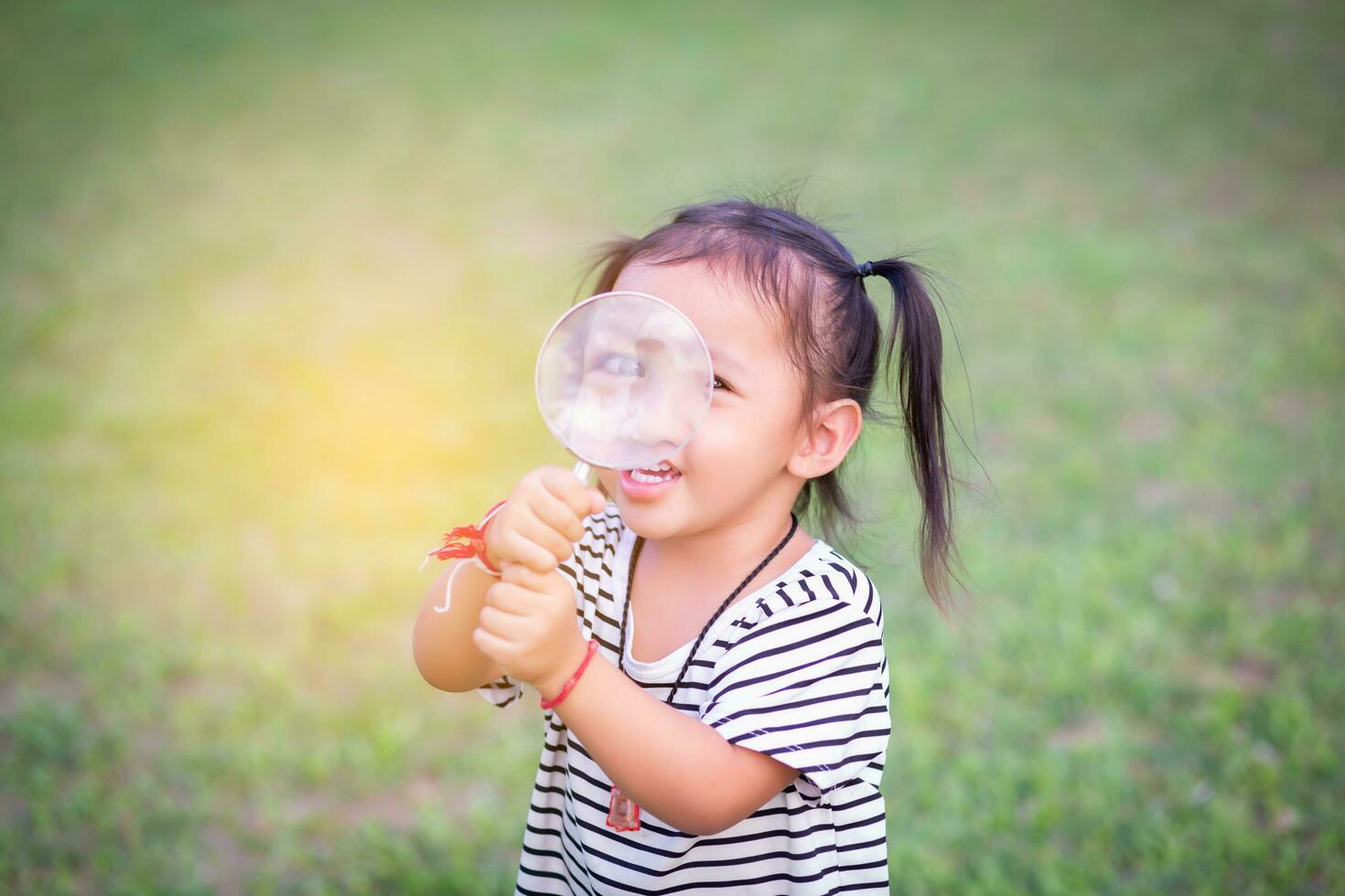 Asian little girl is using magnifying glass to play in the park.SSTKHome photo