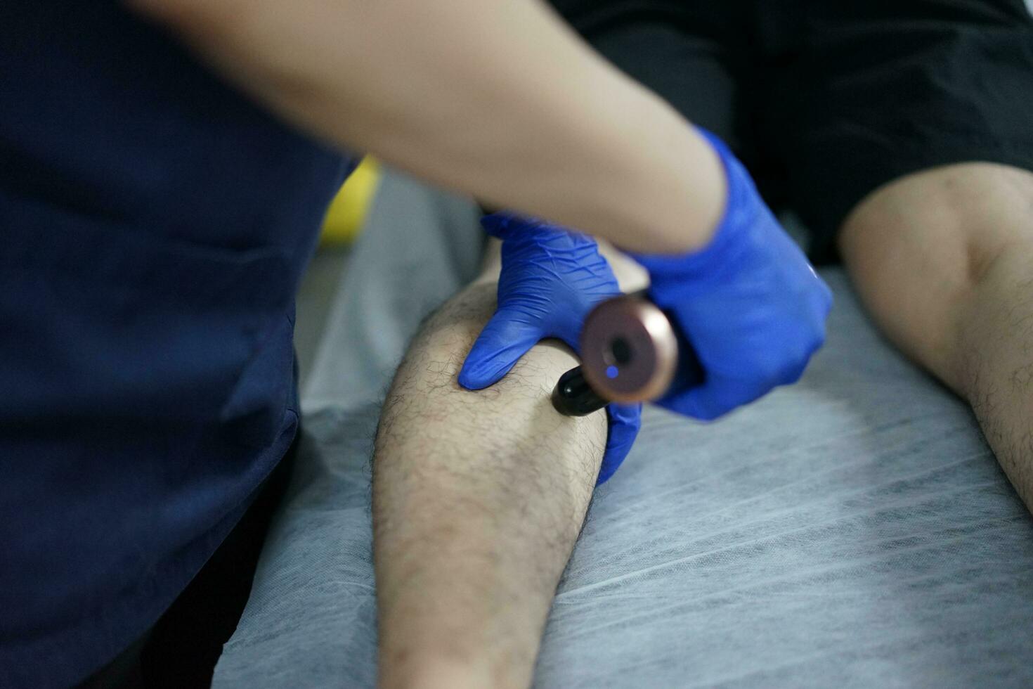 Muscle massage after a hard workout. Physical therapist treats injury of male patient athlete leg. Massage Gun Machine Recovery Therapy And Stimulation photo