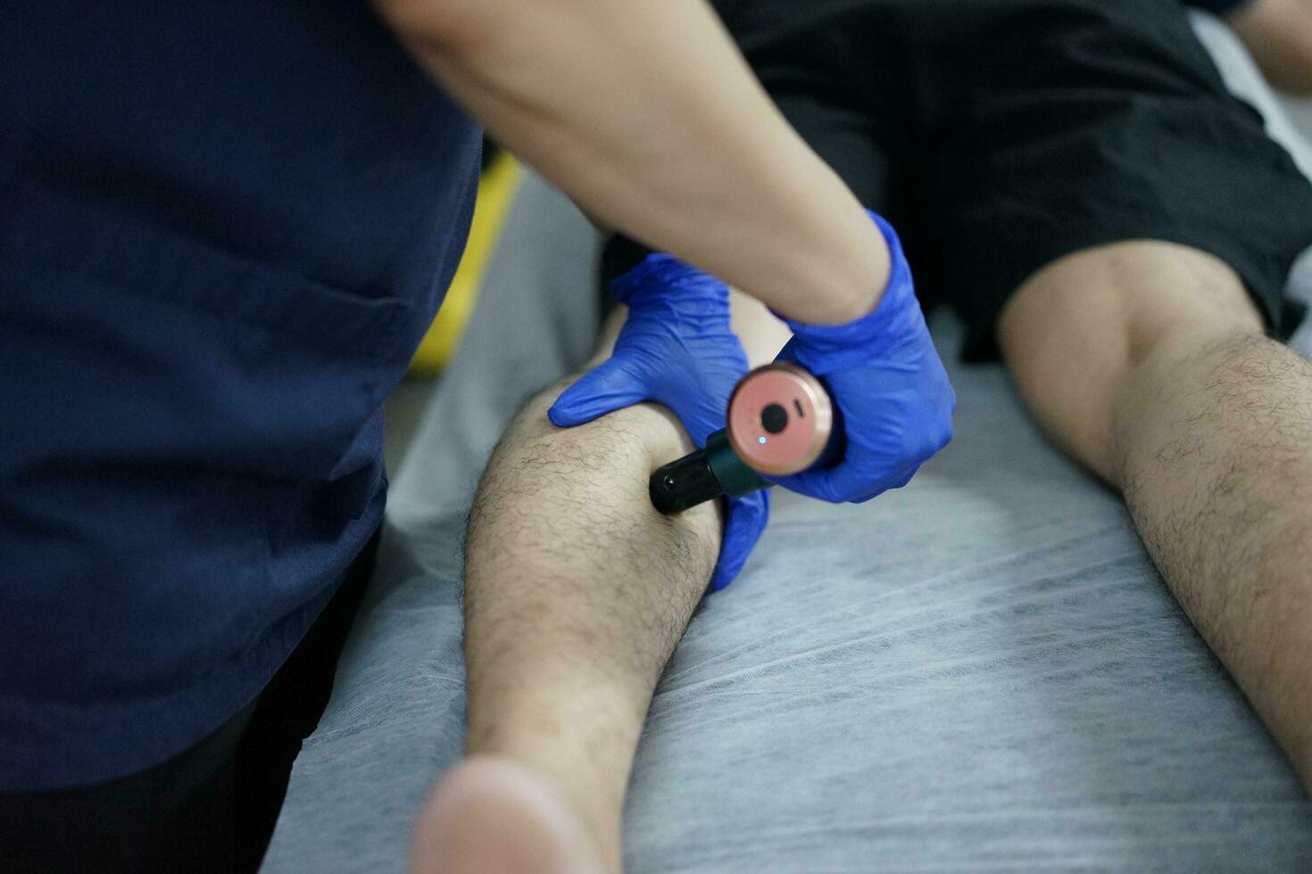 músculo masaje después un difícil ejercicio. físico terapeuta trata lesión de masculino paciente atleta pierna. masaje pistola máquina recuperación terapia y estímulo foto