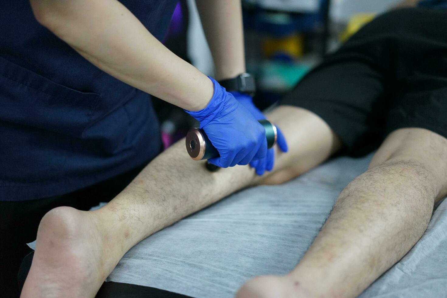 músculo masaje después un difícil ejercicio. físico terapeuta trata lesión de masculino paciente atleta pierna. masaje pistola máquina recuperación terapia y estímulo foto