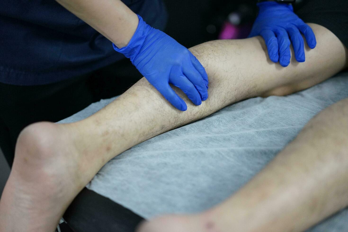 músculo masaje después un difícil ejercicio. físico terapeuta trata lesión de masculino paciente atleta pierna. masaje pistola máquina recuperación terapia y estímulo foto