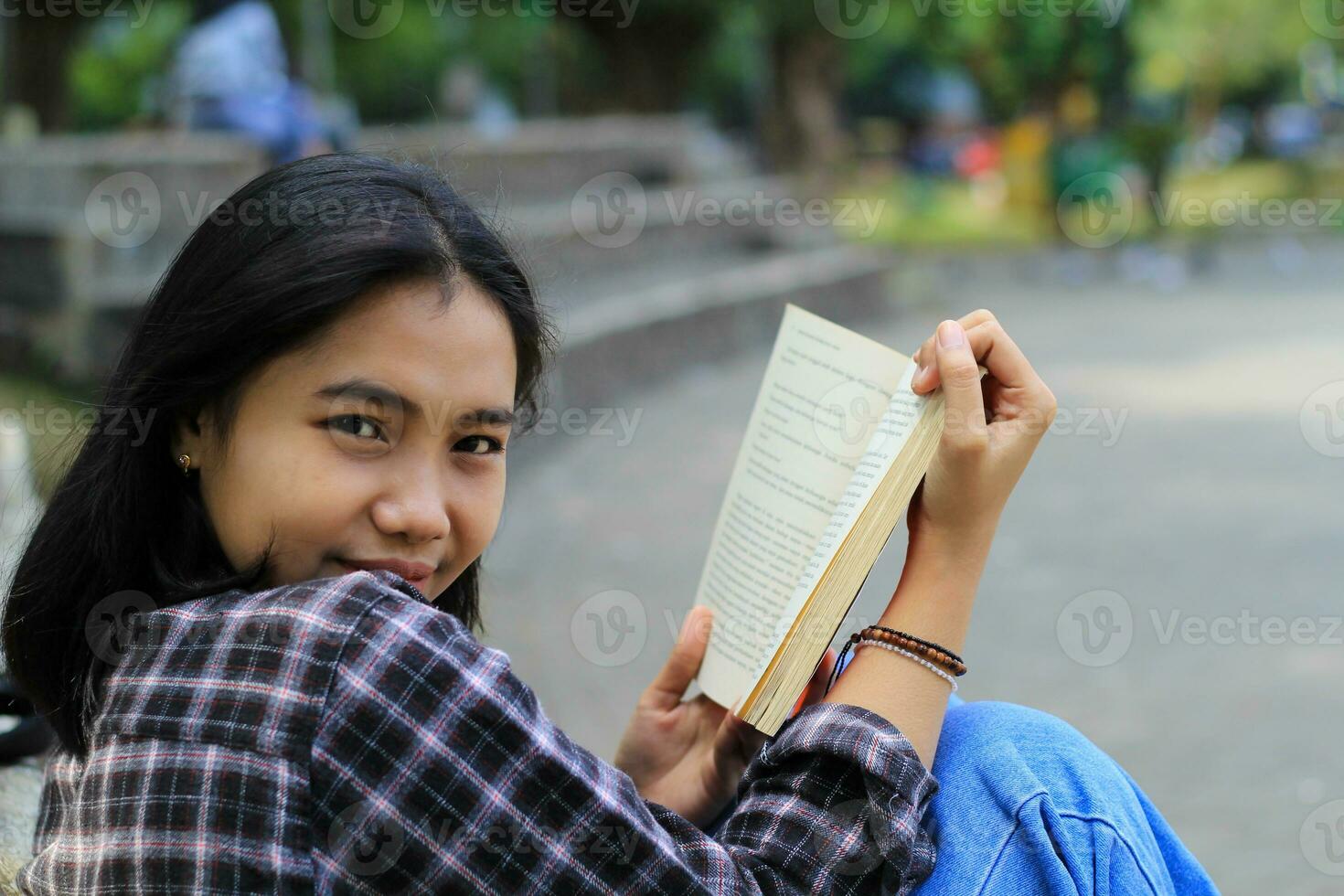 happy young asian woman college student with smiling face enjoy read a book for exam in the park photo