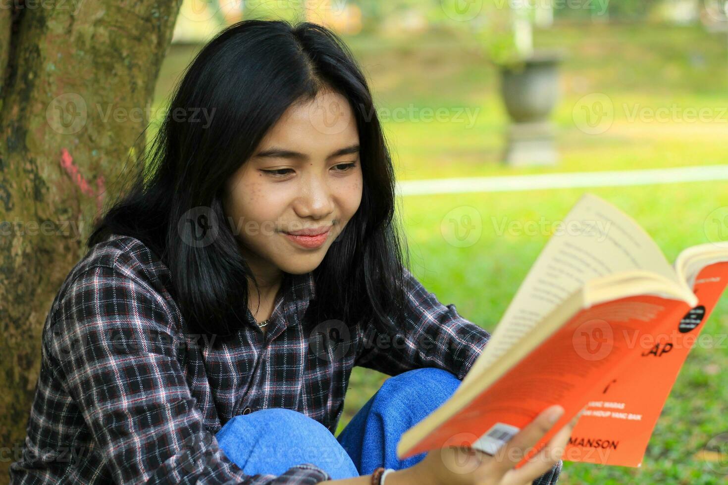 happy and succes female asian college student enjoying read a book in the park photo