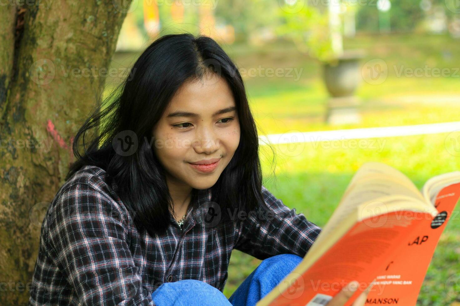 happy and succes female asian college student enjoying read a book in the park photo