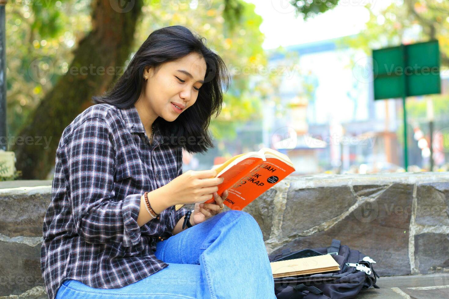 happy cheerful asian female student reading a book and laughing enjoying vacation photo