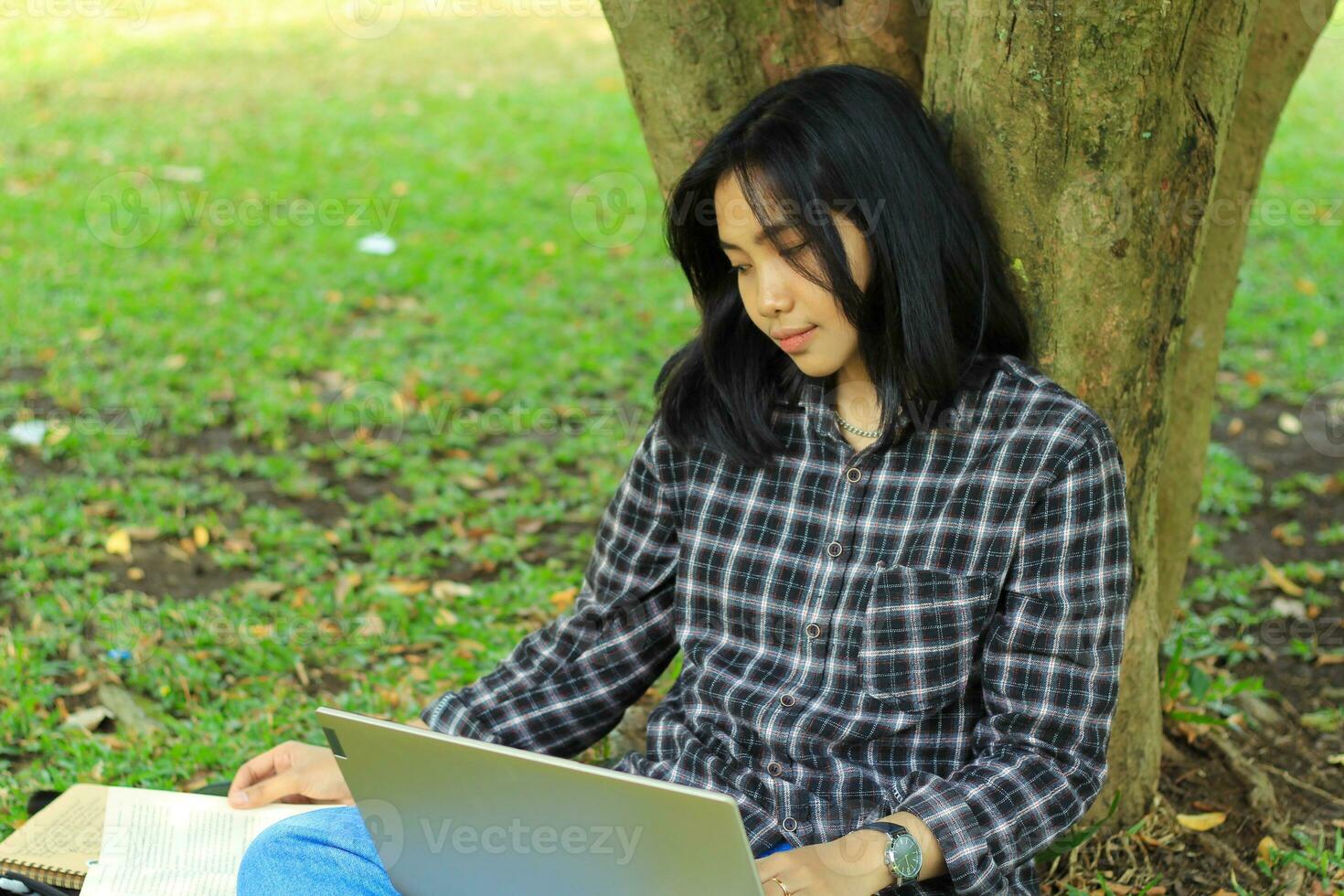 portrait of focused young asian woman surfing internet using laptop to working remotely, read book, and writing in notebook. attractive asian student study in outdoors photo