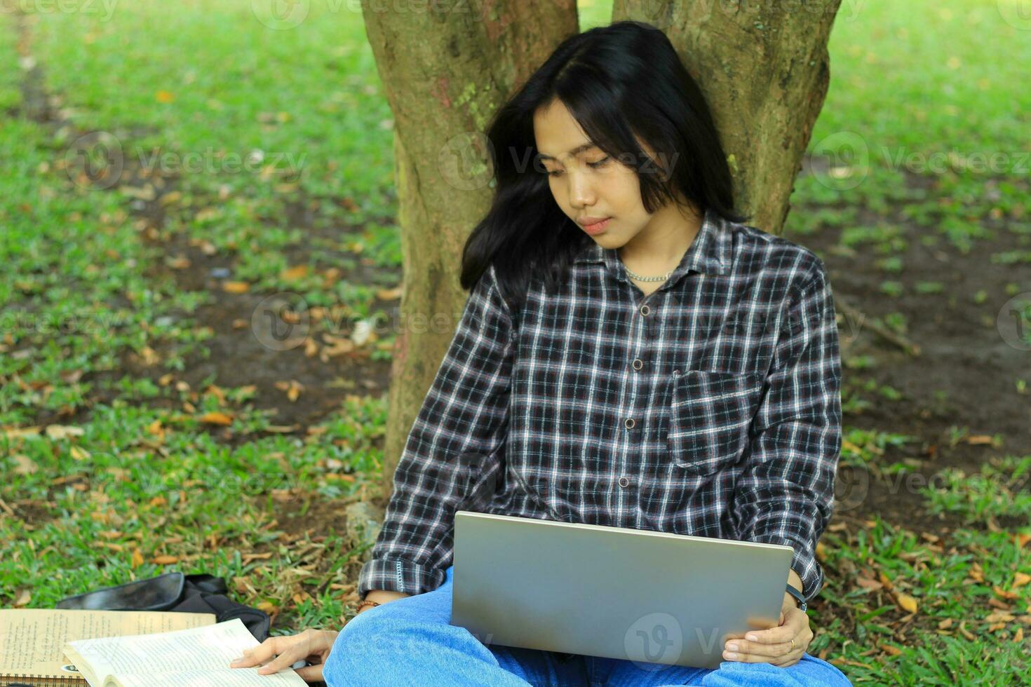 portrait of focused young asian woman surfing internet using laptop to working remotely, read book, and writing in notebook. attractive asian student study in outdoors photo