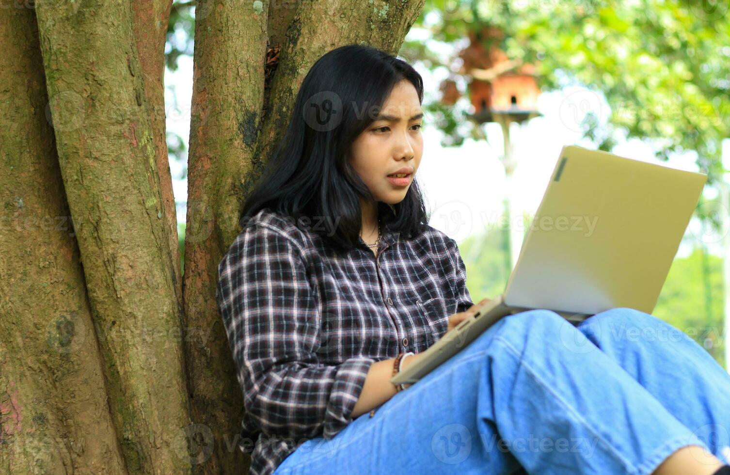 happy young asian woman focused using laptop  working remotely and browsing in social media in comfortable outdoors space photo