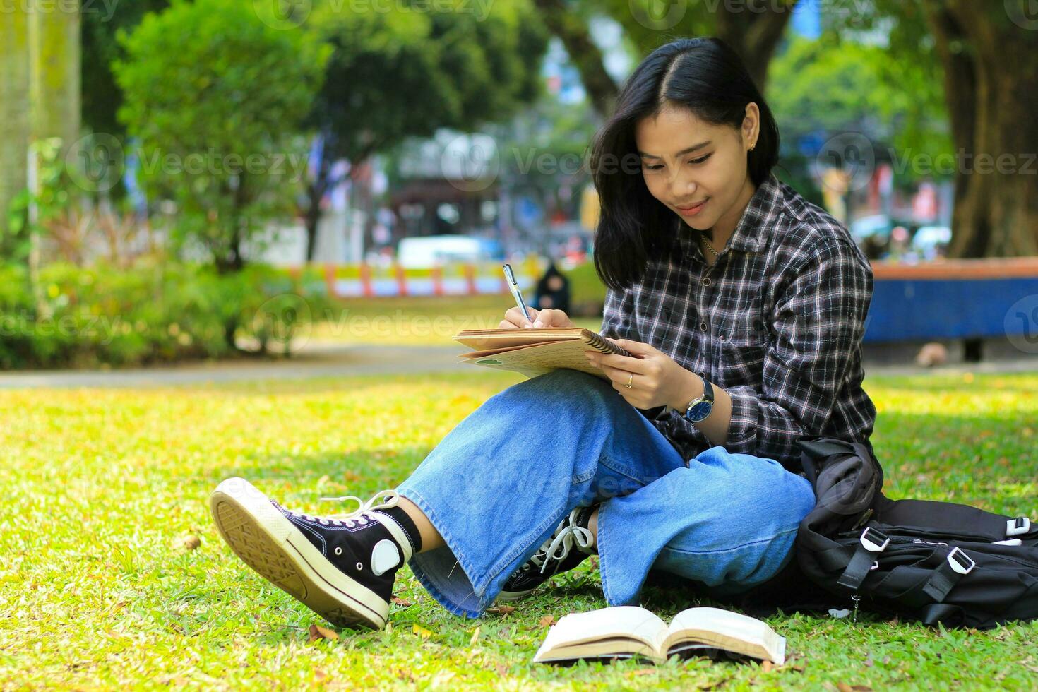 smiling asian beautiful young woman enjoy writing to do list and idea in notebook in outdoors city park photo