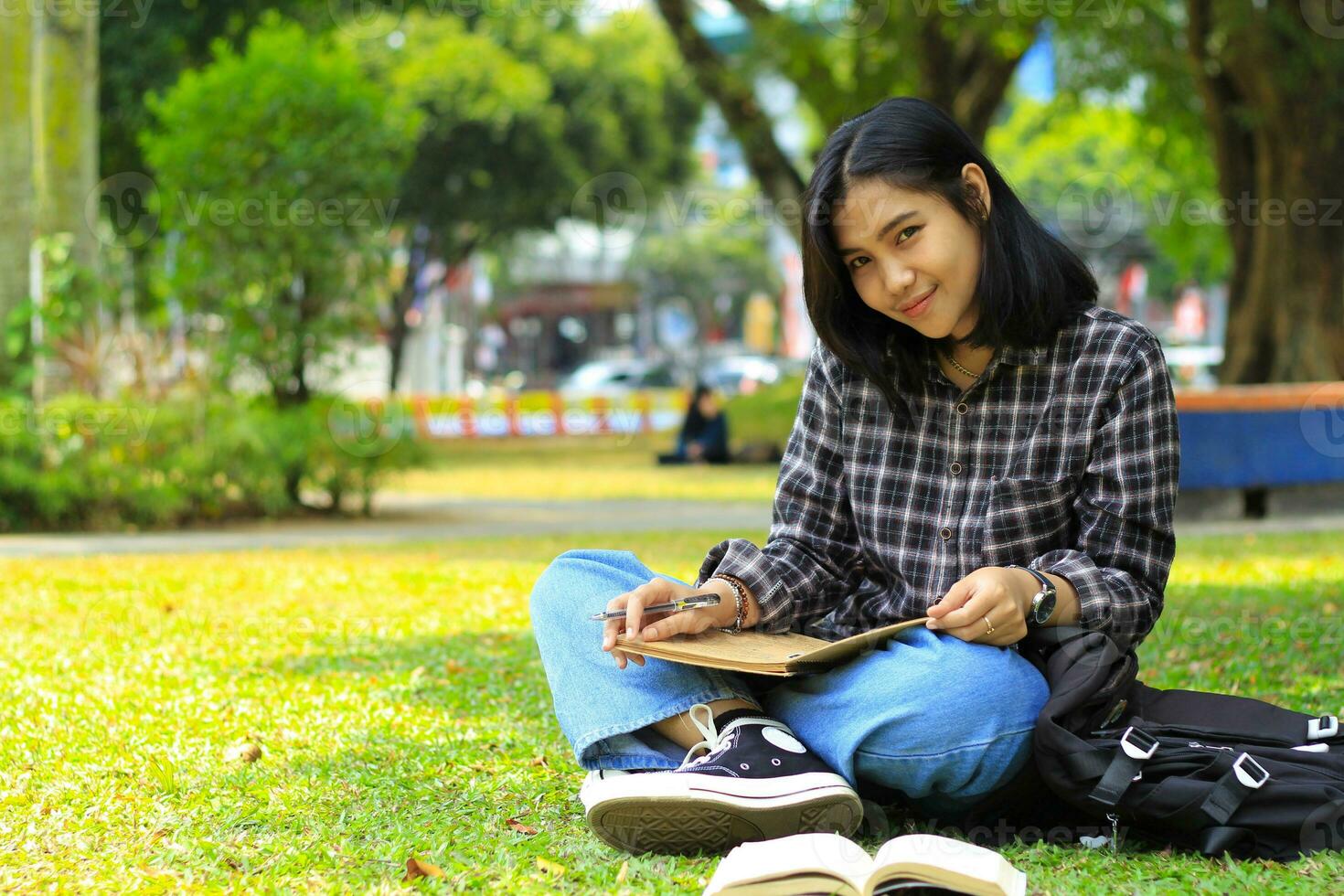 smart happy young asian woman smiling and writing schedule in notebook with a pen study for exam looking at camera photo