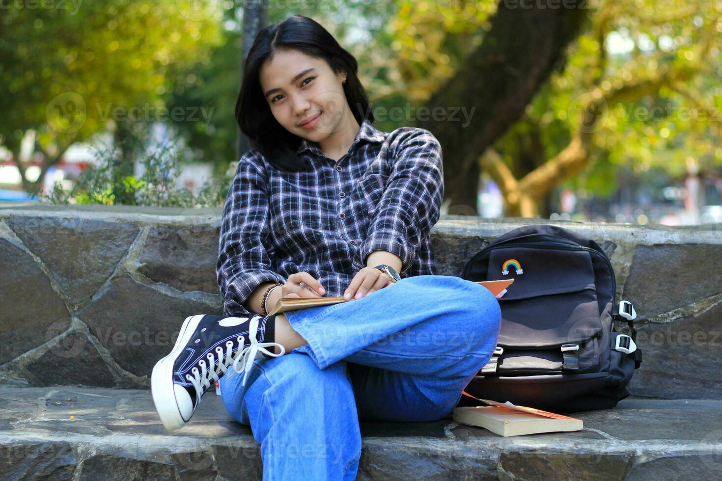 smiling attractive asian young woman writing to do list and organizing her job on notebook in city park photo