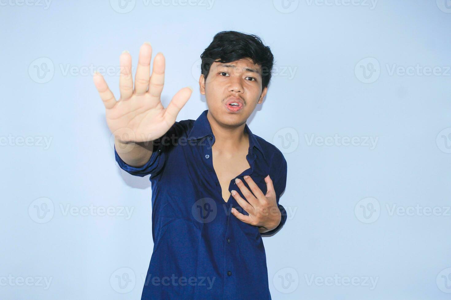 asustado asiático hombre es aumento su manos como detener señales gesto y sostener su cofre sensación dolor de corazón ataque vestir abierto camisa foto