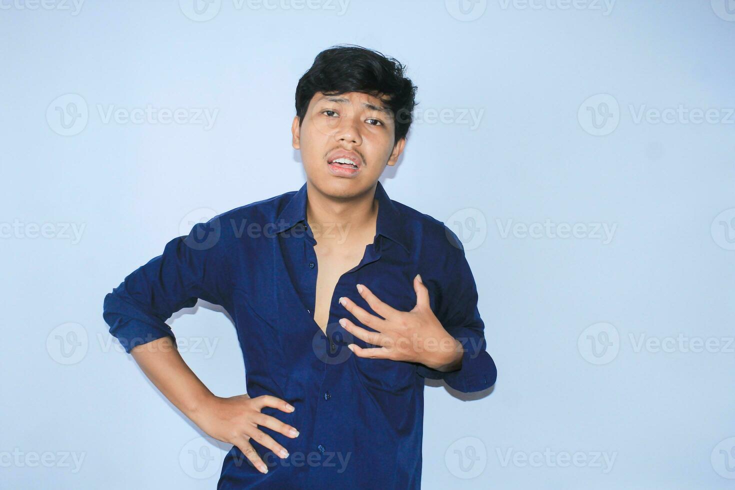 terminado hora asiático joven hombre oficina trabajador es cansado con mano en cintura y sostener su cofre obtener corazón enfermedades síntomas foto