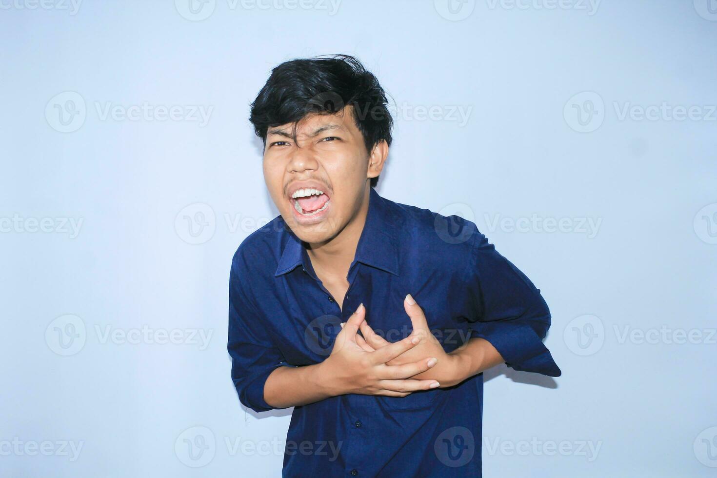 asiático hombre oficina trabajador gritando y conmovedor su cofre sufrimiento desde corazón ataque dolor vistiendo Armada camisa, aislado blanco foto