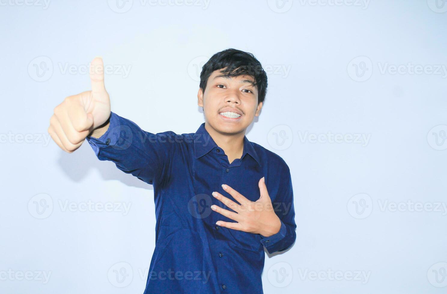 proud young asian man smiling with grateful face for survived from heart attack and has recovery is holding chest with thunbs up wearing navy shirt photo